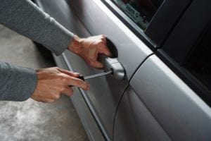 man attempting to open car door with a screwdriver
