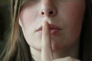 Close up of a woman's face holding her finger to her lips for silence